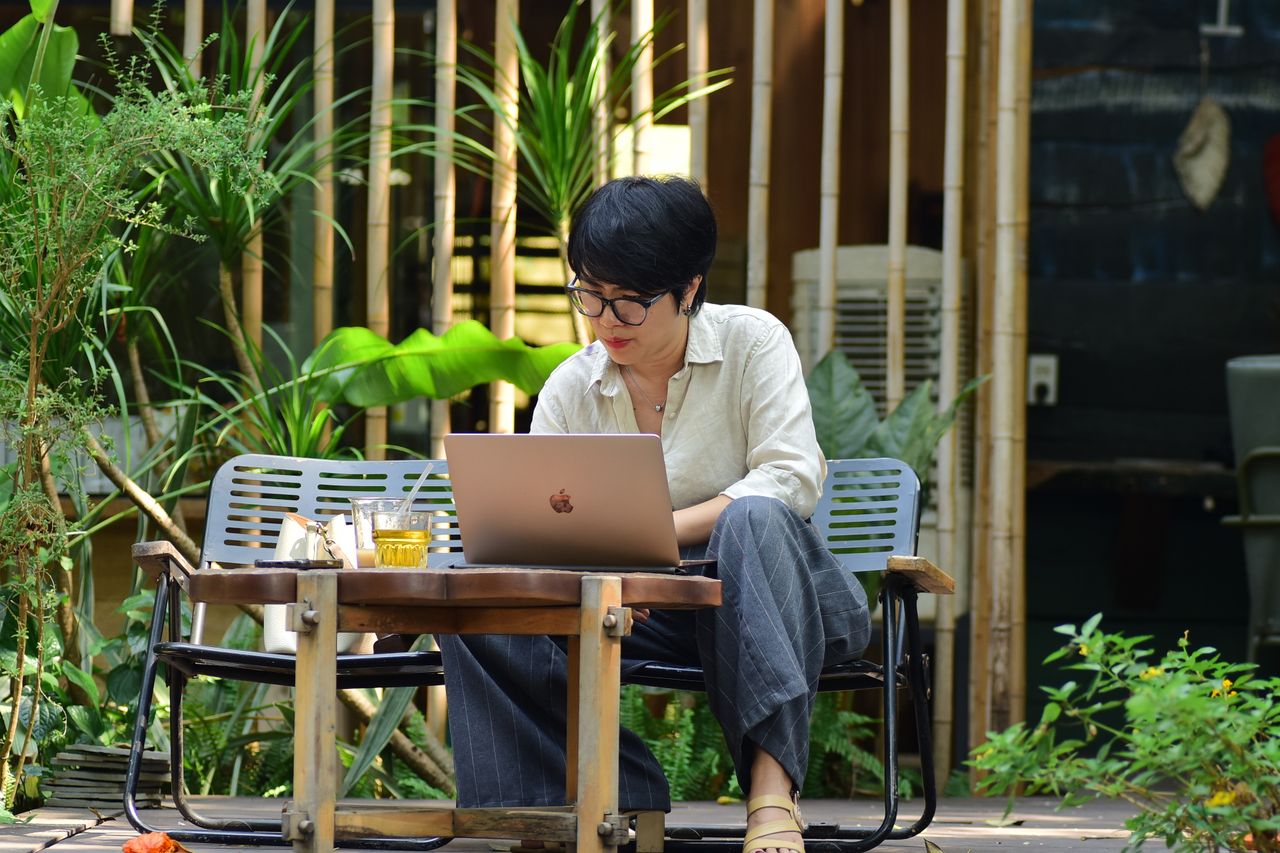 Woman working on a laptop in a lush outdoor café setting.