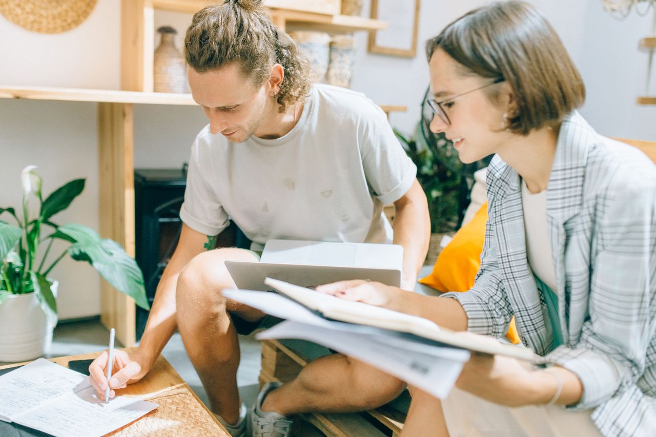 Two young professionals working together in a modern indoor setting, discussing ideas and taking notes.